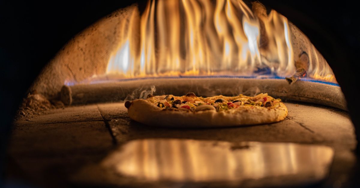 A delicious pizza baking in a traditional wood-fired oven with vibrant flames.