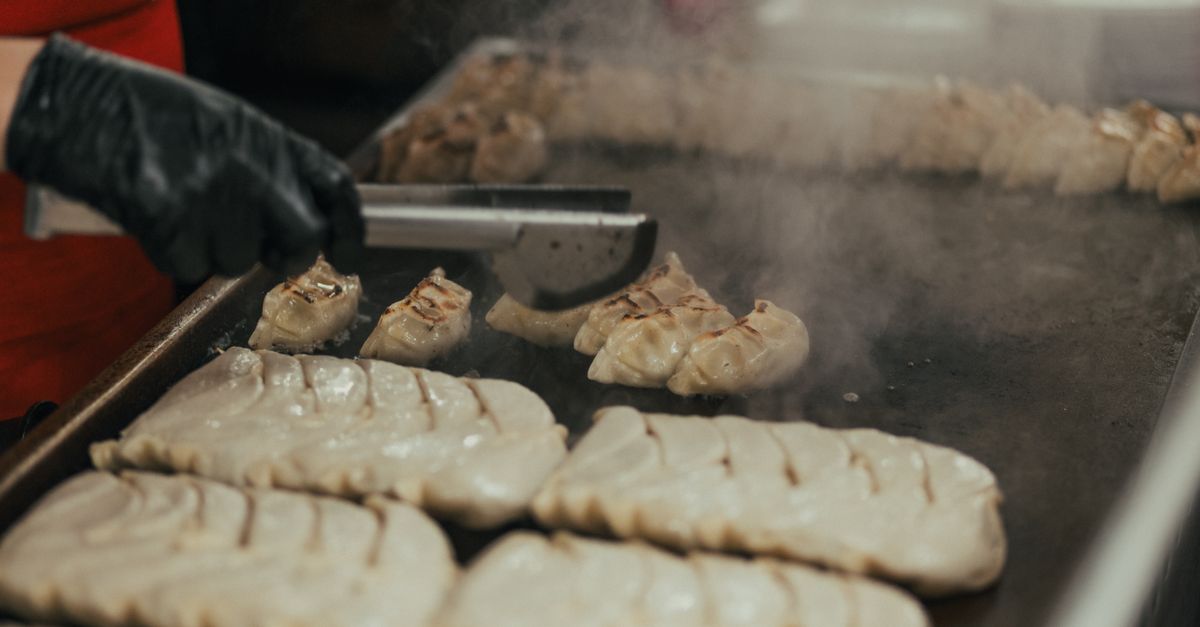 Close-up of a chef cooking dumplings on a griddle in a commercial kitchen.